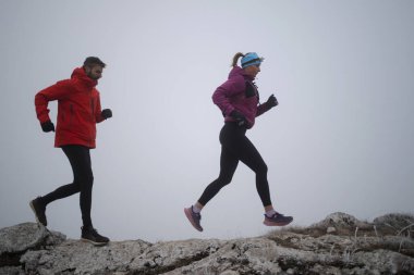 Sabahın erken saatlerinde dağın tepesinde koşan atlet çift patikası. Gökyüzü koşma konsepti, arka planda gökyüzü varken sınırda koşmak tehlikeli. Sağlıklı yaşam, kardiyo egzersizi, spor.