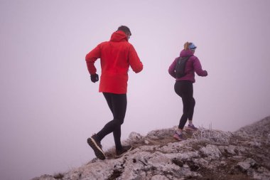 Sabahın erken saatlerinde dağın tepesinde koşan atlet çift patikası. Gökyüzü koşma konsepti, arka planda gökyüzü varken sınırda koşmak tehlikeli. Sağlıklı yaşam, kardiyo egzersizi, spor.