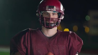 Profesyonel Amerikan futbolcusunun portresi miğferli, dramatik bir ışık altında maça hazır kusuyor. Takım oyunu ve ekstrem spor ruhu iş dünyası liderliği kavramı. Sinema yavaşlığı