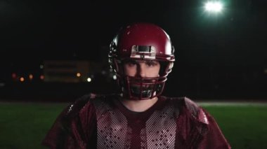 Stadyum ışıkları altında yoğun gece eğitimi sırasında çekilen tam teçhizatlı bir Amerikan futbolcusunun dinamik portresi.