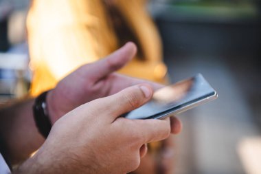 İş adamının yakın plan fotoğrafı, akıllı telefonunu açık havada kullanır ve modern profesyonel hayatta teknolojinin ve hareketliliğin kusursuz bütünlüğünü gösterir.