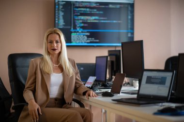 Bilgisayarlarla çevrili bir programcı ofisinde oturan bir iş kadını uzmanlığını ve teknolojiye olan bağlılığını gösteriyor..