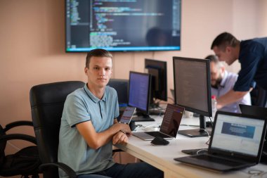 Genç bir programcı ofisinde masasında oturmuş, akıllı telefonlar için yenilikçi yeni uygulamaları test etmeye odaklanmış, yaratıcılık ve teknoloji ruhunu somutlaştırıyor..