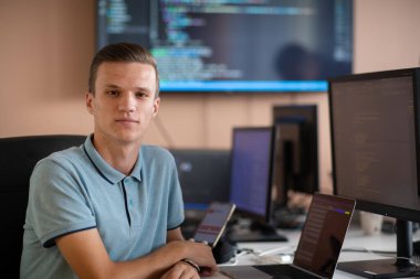 Genç bir programcı ofisinde masasında oturmuş, akıllı telefonlar için yenilikçi yeni uygulamaları test etmeye odaklanmış, yaratıcılık ve teknoloji ruhunu somutlaştırıyor..