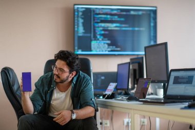 Bir programcı ofisinde otururken akıllı telefon uygulamalarını özenle test eder.