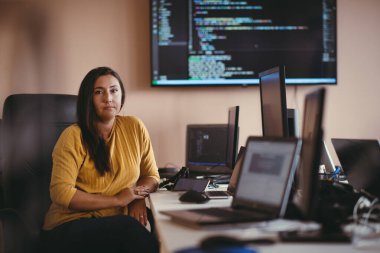 Bilgisayarlarla çevrili bir programcı ofisinde oturan bir iş kadını uzmanlığını ve teknolojiye olan bağlılığını gösteriyor.