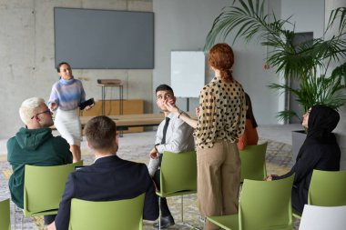 Çeşitli iş adamları modern bir ofiste dikkatle oturup, bir eğitmenin önderliğindeki bir eğitim oturumunda aktif olarak en son teknolojik gelişmelere odaklanırlar.