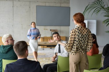 Çeşitli iş adamları modern bir ofiste dikkatle oturup, bir eğitmenin önderliğindeki bir eğitim oturumunda aktif olarak en son teknolojik gelişmelere odaklanırlar.