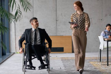 Director in a Wheelchair Engaging in a Business Discussion with a Colleague While Navigating a Modern Office. clipart