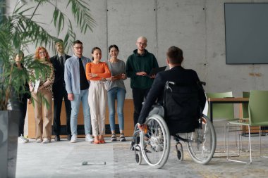 Çağdaş bir ofiste tekerlekli sandalyede müdürle işbirliği yapan çok ırklı iş adamları..