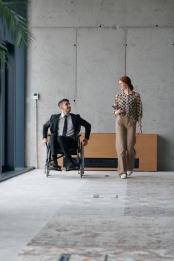 Bir meslektaşımla iş görüşmeleri tartışırken tekerlekli sandalyede ofisi gezen bir yönetmen..