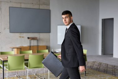 Siyah takım elbiseli kararlı bir işadamı ofisin içinde güven içinde yürüyor, profesyonelliği somutlaştırıyor ve yeni zorluklara doğru ilerlerken odaklanıyor.. 