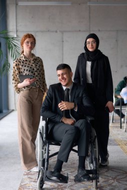 Çeşitli bir iş ekibi güven içinde poz veriyor. Aralarında tekerlekli sandalyede oturan gülümseyen bir yönetmen de var. Birinde tesettür takan, diğerinde tablet tutan iki profesyonel meslektaşı var.