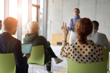 Çeşitli iş adamları modern bir ofiste dikkatle oturup, bir eğitmenin önderliğindeki bir eğitim oturumunda aktif olarak en son teknolojik gelişmelere odaklanırlar.
