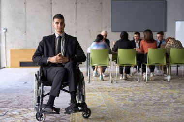 Business Director in a Suit Using a Wheelchair with Colleagues Conducting a Meeting Behind Him. clipart