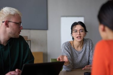Genç, çeşitli bir iş ekibi modern bir ofiste birlikte oturuyor, fikir ve iş planlarını paylaşıyor, gelecekteki başarı için işbirliği ve yenilikleri teşvik ediyor.