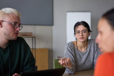 Genç, çeşitli bir iş ekibi modern bir ofiste birlikte oturuyor, fikir ve iş planlarını paylaşıyor, gelecekteki başarı için işbirliği ve yenilikleri teşvik ediyor.