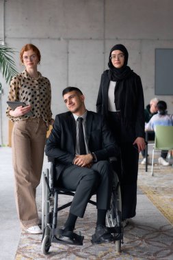 Çeşitli bir iş ekibi güven içinde poz veriyor. Aralarında tekerlekli sandalyede oturan gülümseyen bir yönetmen de var. Birinde tesettür takan, diğerinde tablet tutan iki profesyonel meslektaşı var.