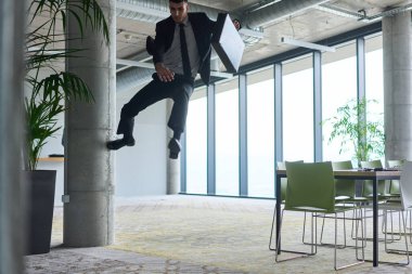 Modern bir ofise kendinden geçmiş bir şekilde atlayan bir işadamı, elinde bir evrak çantasıyla, başarı ve zafer anını kutluyor.