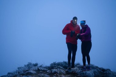 Eğitimden sonra nefes almaktan sıkılan koşucular, teknoloji sporu saatlerine bakmaktan, kalp atış hızı verilerini ve navigasyonlarını kontrol etmekten bıktılar. İki sporcu bir dağda birlikte koşuyor..
