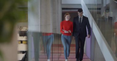 Modern bir girişim şirketinin dinamik ortamında, yönetici genç iş arkadaşı ile yürürken bir tartışma içine girer, işbirliği ve yenilik ruhunu yansıtır.