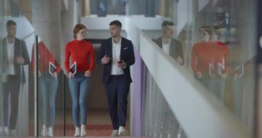 Modern bir girişim şirketinin dinamik ortamında, yönetici genç iş arkadaşı ile yürürken bir tartışma içine girer, işbirliği ve yenilik ruhunu yansıtır.