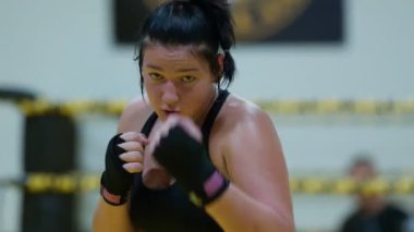 Kickboks yapan kadın boksör yumruklarını çalıştırırken kız hızlı saldırırken spor salonunda günlük antrenman yapıyor. Yüksek kalite 8K görüntü