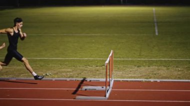 Stadyuma atletik zinde bir çift erkek ve kadın fırlatılıyor. Sıcak bir yaz öğleden sonrasında engellerin üzerinden atlamak. Yavaş Hareket İzleme Görüntüsü. 