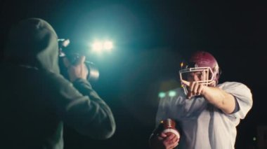 Takım üniformalı, pedli ve kasklı Amerikalı futbolcu kameraya doğru bakıyor. Güçlü, aksiyon dolu, takım ruhunu yakalayan ve oyun için hazır olan bir görüntü. Sinematik ağır çekim