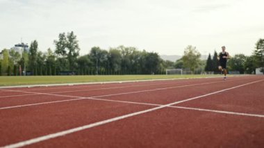 Güneşli bir sabahta atletizm pistinde koşan genç bir sporcunun dikey videosu. Spor anlayışı ve azim. Yüksek kalite 4k görüntü