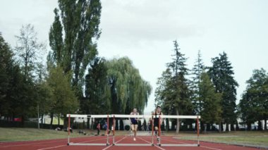 Stadyuma atletik zinde bir çift erkek ve kadın fırlatılıyor. Sıcak bir yaz öğleden sonrasında engellerin üzerinden atlamak. Yavaş Hareket İzleme Görüntüsü. 