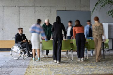 A diverse business team, working urgently around a conference table, collaborates on a meeting while their director, seated in a wheelchair, waits for their input.  clipart