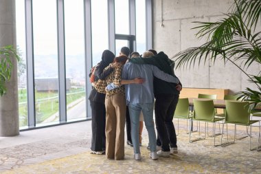 A diverse group of professionals standing in a supportive circle, embracing each other in a modern office space filled with natural light clipart