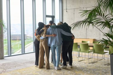 A diverse group of professionals standing in a supportive circle, embracing each other in a modern office space filled with natural light clipart