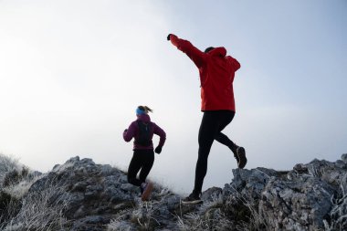 Sabahın erken saatlerinde dağın tepesinde koşan atlet çift patikası. Gökyüzü koşma konsepti, arka planda gökyüzü varken sınırda koşmak tehlikeli. Sağlıklı yaşam, kardiyo egzersizi, spor.