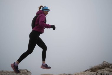 Gökyüzü koşuyor ya da bir dağın tepesinde egzersiz yapan bir kadını takip ediyor. Açık havada antrenman yapan koşucu bir kadın aktif ve zinde bir hayat sürüyor. Siluet sabahın erken saatlerinde.