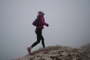 Gökyüzü koşuyor ya da bir dağın tepesinde egzersiz yapan bir kadını takip ediyor. Açık havada antrenman yapan koşucu bir kadın aktif ve zinde bir hayat sürüyor. Siluet sabahın erken saatlerinde.