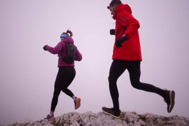 Sabahın erken saatlerinde dağın tepesinde koşan atlet çift patikası. Gökyüzü koşma konsepti, arka planda gökyüzü varken sınırda koşmak tehlikeli. Sağlıklı yaşam, kardiyo egzersizi, spor.
