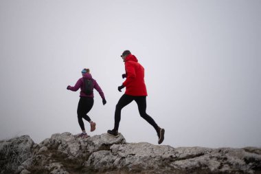 Sabahın erken saatlerinde dağın tepesinde koşan atlet çift patikası. Gökyüzü koşma konsepti, arka planda gökyüzü varken sınırda koşmak tehlikeli. Sağlıklı yaşam, kardiyo egzersizi, spor.