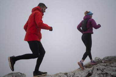 Sabahın erken saatlerinde dağın tepesinde koşan atlet çift patikası. Gökyüzü koşma konsepti, arka planda gökyüzü varken sınırda koşmak tehlikeli. Sağlıklı yaşam, kardiyo egzersizi, spor.