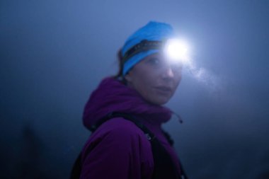 Geceleri engebeli dağ arazisinde koşan bir kadın patikası, bir far ışığıyla aydınlatılan yolu.