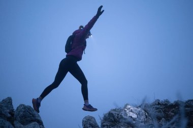 Geceleri engebeli dağ arazisinde koşan bir kadın patikası, bir far ışığıyla aydınlatılan yolu.