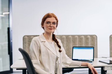 A modern businesswoman with striking orange hair sitting confidently in a contemporary office, accompanied by her laptop, embodying professionalism, creativity, and success in a technology-driven clipart