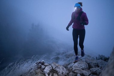 Geceleri engebeli dağ arazisinde koşan bir kadın patikası, bir far ışığıyla aydınlatılan yolu.
