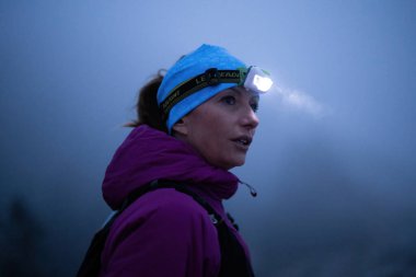 Geceleri engebeli dağ arazisinde koşan bir kadın patikası, bir far ışığıyla aydınlatılan yolu.