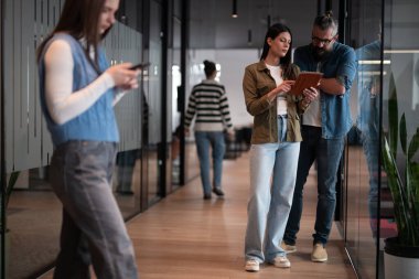Üst düzey bir hipster akıl hocası ve Avrupalı bir lider, modern bir çalışma alanında tablet üzerinde çalışırken, arka planda yoğun meslektaşlar çalışırken güvenli bir şekilde işbirliği yaparak bir projeyi tartışıyorlar.