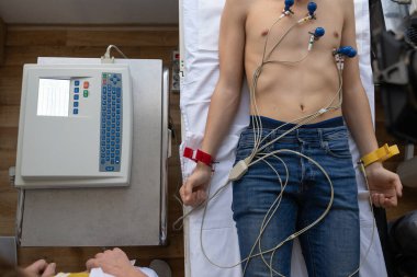 Kadın bir doktor, hastane odasında genç bir adama EKG çeker. Rutin bir kontrol sırasında kalp sağlığını dikkatle izler.