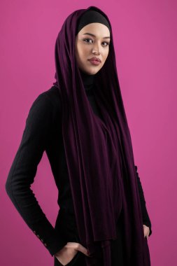 Başörtülü çarpıcı bir Müslüman kadın zarif bir şekilde stüdyoda pembe bir arka plana karşı poz veriyor, zarafet ve güven yayıyor.. 