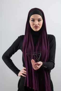 Kendine güveni tam bir Müslüman kadın şık mor bir başörtüsü ve yüzen geometrik bir yapıyla poz vererek modern ve sanatsal bir portre yaratıyor.. 