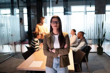 Modern bir ofiste kendine güvenen bir iş kadını. Girişimsel bir iş toplantısında çeşitli takımlar arka planda işbirliği yaparak açık uzay ofis ortamında iş birliği yapıyorlar. Şirket takım çalışması